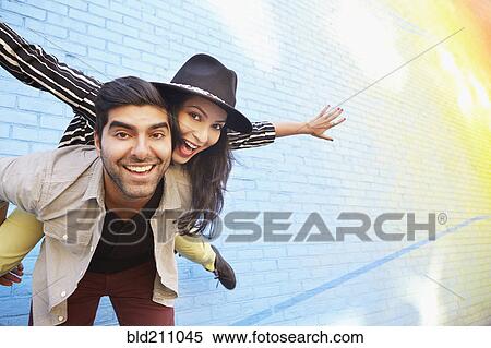 Stock Photography - Indian couple piggybacking along brick wall. Fotosearch