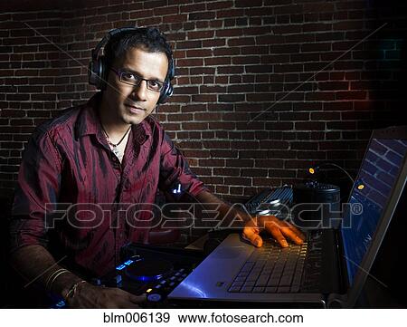 Stock Photo - Indian man in headphones with laptop. Fotosearch