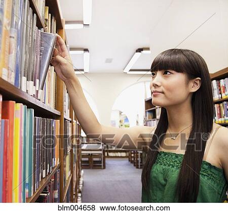 Stock Photo - Japanese woman looking for book in library. Fotosearch