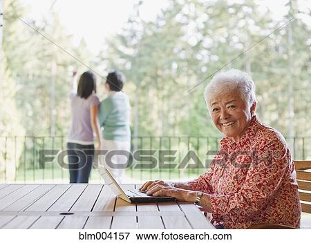 Stock Photo - Japanese woman using laptop on patio. Fotosearch