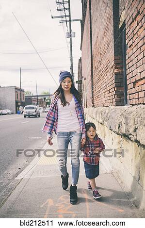Stock Image - Korean mother and daughter holding hands on city street. Fotosearch