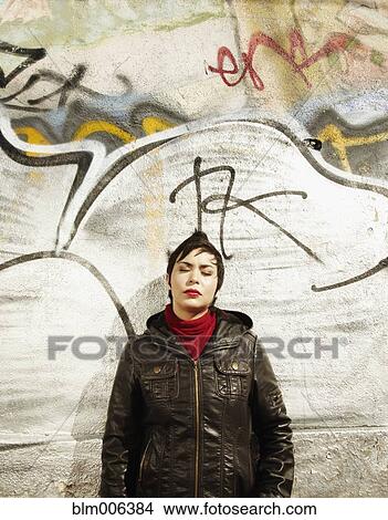Picture - Latin American woman leaning against graffitied wall. Fotosearch