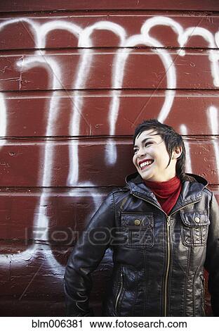 Stock Image - Latin American woman leaning against graffitied wall. Fotosearch
