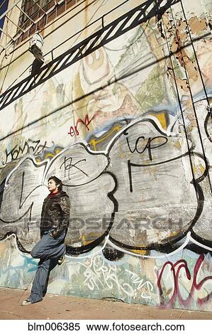 Stock Photography - Latin American woman leaning against graffitied wall. Fotosearch