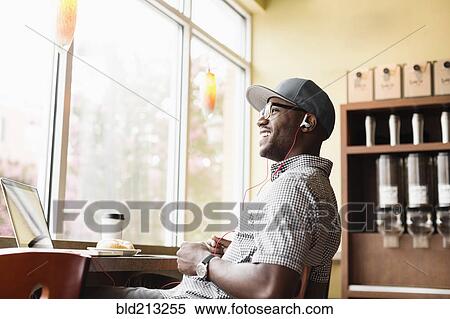 Stock Photography - Laughing Black man using laptop in coffee shop. Fotosearch