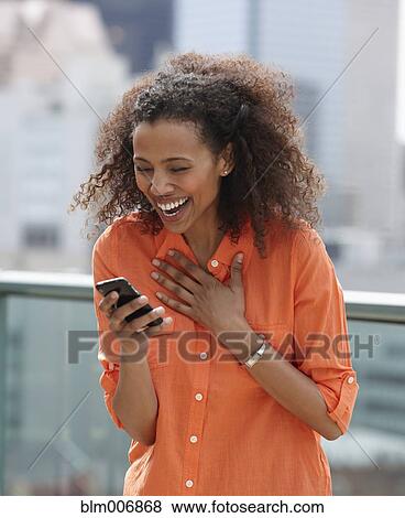 Stock Photo - Laughing Black woman text messaging on cell phone. Fotosearch