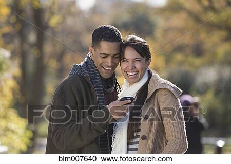 Laughing couple looking at cell phone View Large Photo Image Stock Image - Laughing couple looking at cell phone. Fotosearch