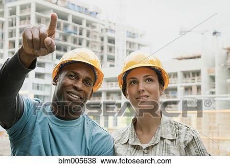 Stock Photo - Man and woman in hard-hats on construction site. Fotosearch