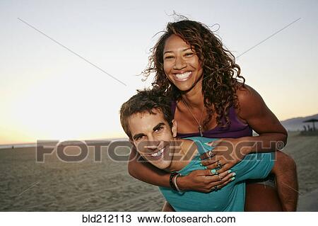 Man carrying girlfriend piggyback on beach View Large Photo Image Stock Image - Man carrying girlfriend piggyback on beach. Fotosearch