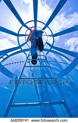 Stock Image - Man climbing water tower ladder. Fotosearch