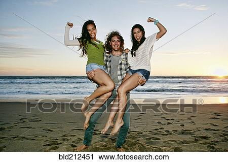 Stock Image - Man holding women on each arm on beach. Fotosearch
