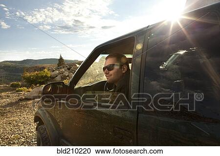 Stock Image - Man sitting in car overlooking rural landscape. Fotosearch