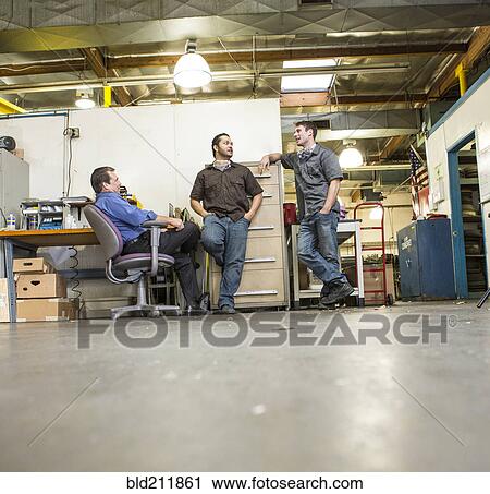 Stock Image - Manager and workers talking in warehouse. Fotosearch