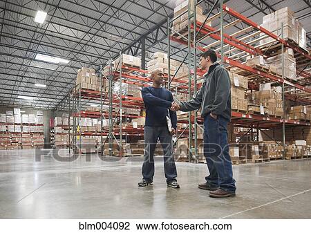 Stock Image - Men shaking hands in warehouse. Fotosearch