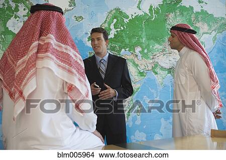 Picture - Middle Eastern businessman talking to men in traditional clothing. Fotosearch