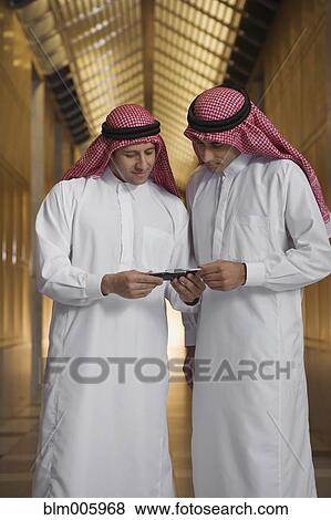 Stock Photo - Middle Eastern men in traditional clothing text messaging on cell phone. Fotosearch