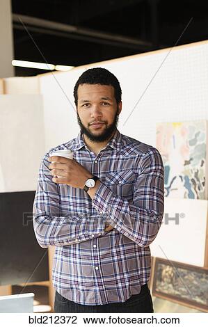 Stock Image - Mixed race artist drinking coffee in studio. Fotosearch