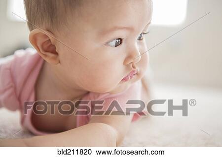 Stock Image - Mixed race baby girl laying on carpet. Fotosearch
