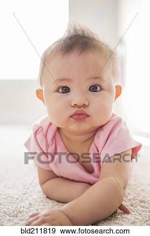 Stock Photo - Mixed race baby girl laying on carpet. Fotosearch