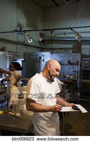 Stock Image - Mixed race bakery owner writing on clipboard. Fotosearch