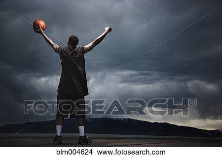 Picture - Mixed race basketball player standing with storm clouds in distance. Fotosearch