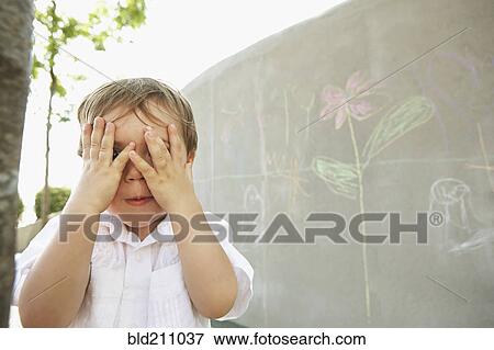 Stock Photo - Mixed race boy covering his eyes outdoors. Fotosearch