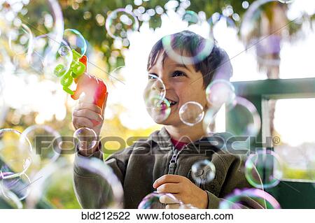 Stock Image - Mixed race boy playing with bubbles outdoors. Fotosearch