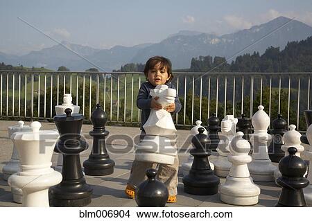 Picture - Mixed race boy playing with large chess pieces. Fotosearch