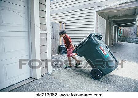 Stock Image - Mixed race boy pulling trash can in driveway. Fotosearch