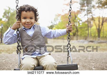 Mixed race boy sitting on swing in park View Large Photo Image Stock Photo - Mixed race boy sitting on swing in park. Fotosearch