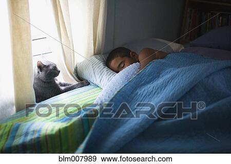 Stock Photo - Mixed race boy sleeping in bed with cat. Fotosearch