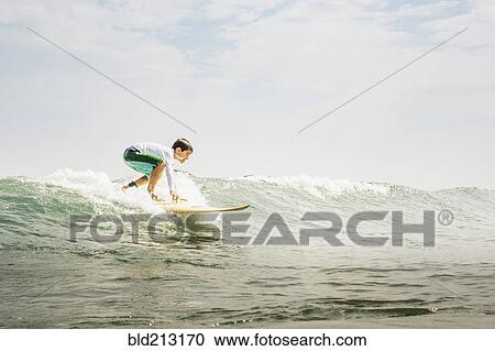 Stock Image - Mixed race boy surfing in waves. Fotosearch