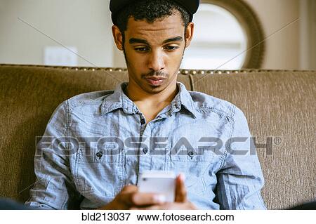Stock Photo - Mixed race boy using cell phone on sofa. Fotosearch