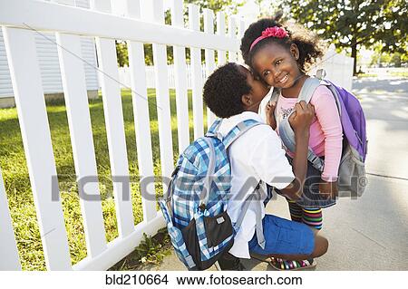 Picture - Mixed race boy whispering in sister's ear. Fotosearch