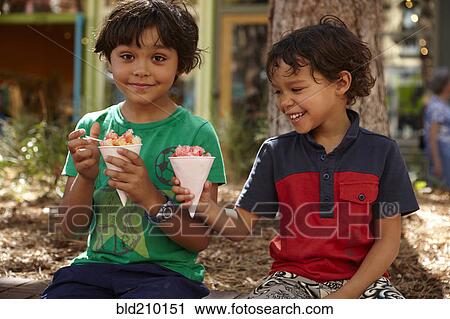 Stock Image - Mixed race boys eating ice cream outdoors. Fotosearch
