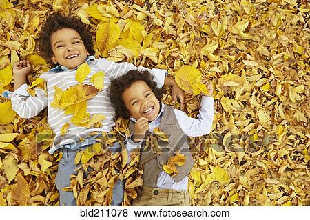 Stock Photo - Mixed race boys laying in yellow autumn leaves. Fotosearch