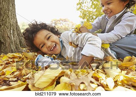 Stock Photo - Mixed race boys playing in yellow autumn leaves. Fotosearch
