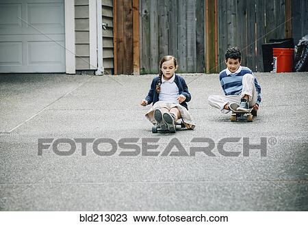 Stock Image - Mixed race brother and sister riding skateboards in driveway. Fotosearch
