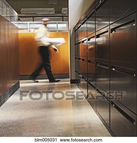 Stock Image - Mixed race businessman carrying blueprints in office. Fotosearch