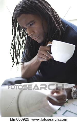 Stock Photography - Mixed race businessman drinking coffee and reviewing report. Fotosearch