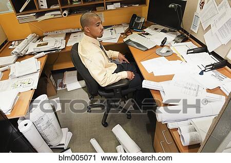 Stock Image - Mixed race businessman sitting at messy desk. Fotosearch