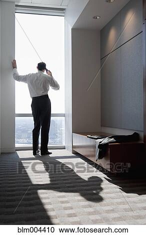 Stock Image - Mixed race businessman talking on cell phone at window. Fotosearch