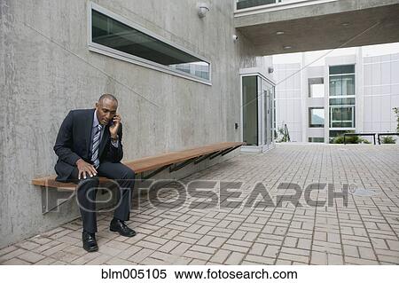 Stock Photography - Mixed race businessman talking on cell phone in courtyard. Fotosearch