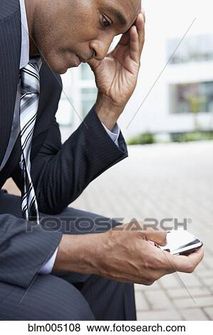 Stock Photo - Mixed race businessman text messaging on cell phone. Fotosearch