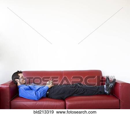 Stock Photo - Mixed race businessman using cell phone on sofa. Fotosearch