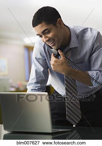Mixed race businessman using laptop and talking on telephone View Large Photo Image Stock Photo - Mixed race businessman using laptop and talking on telephone. Fotosearch