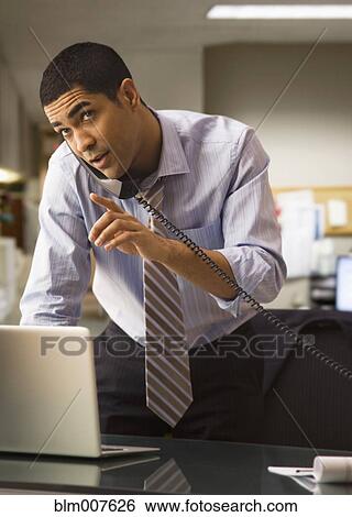 Stock Photograph - Mixed race businessman using laptop and talking on telephone. Fotosearch