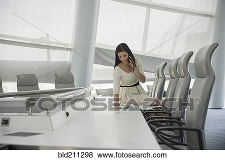 Stock Photo - Mixed race businesswoman on cell phone in conference room. Fotosearch