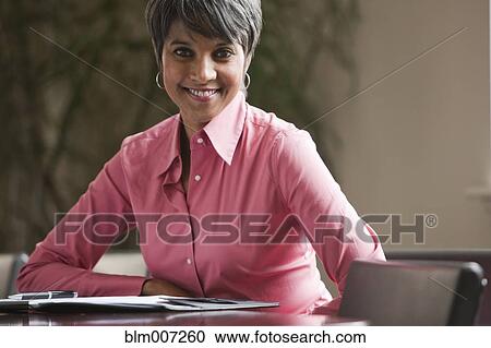 Mixed race businesswoman sitting at table View Large Photo Image Stock Image - Mixed race businesswoman sitting at table. Fotosearch
