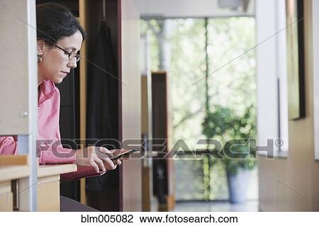 Stock Image - Mixed race businesswoman text messaging on cell phone in office. Fotosearch